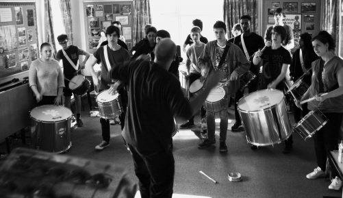 Group of people playing samba instruments with leader at the front