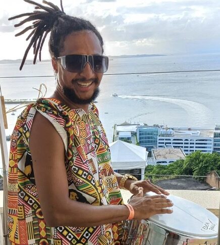 Vinicius, workshop leader and percussionist, playing a drum overlooking a beach